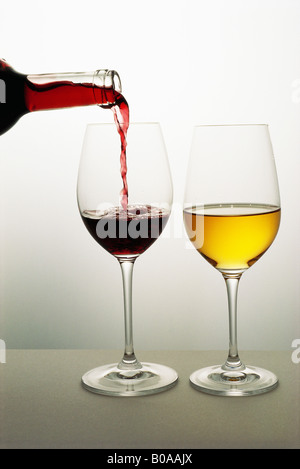 Two wine glasses, red wine being poured into one, white wine in the other Stock Photo