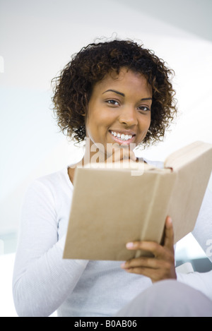 Woman holding book in one hand, other hand under chin, smiling at camera Stock Photo