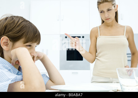 Boy pouting at kitchen table, mother shaking her finger Stock Photo