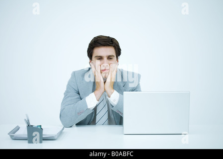 Businessman sitting at desk, holding head in hands, frowning Stock Photo