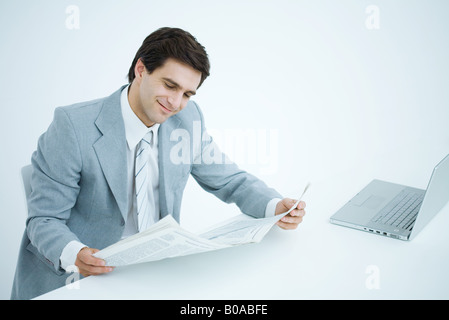 Businessman sitting at desk, reading newspaper Stock Photo