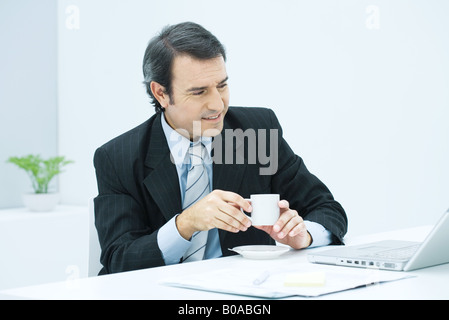Mature businessman sitting at desk with cup of coffee, smiling Stock Photo