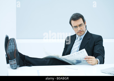 Businessman sitting with feet up, reading newspaper Stock Photo