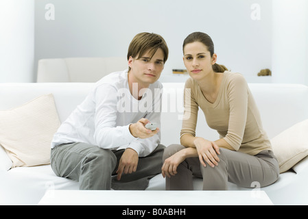 Young couple watching TV, pointing remote control at camera