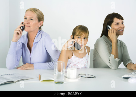 Mother and two daughters sitting at table, each using cell phone, smiling Stock Photo