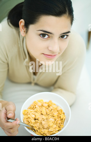 Young woman lying on stomach, holding cereal bowl, looking at camera Stock Photo