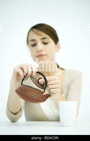 Young woman looking at teapot, lifting lid, focus on foreground Stock Photo