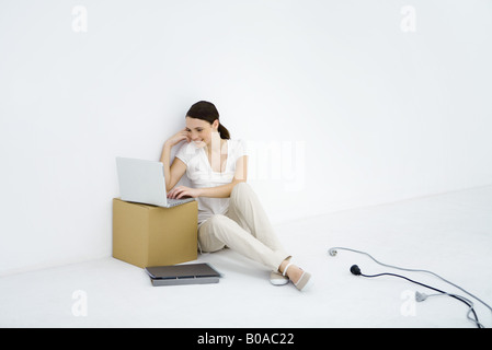 Young woman sitting on the ground, using laptop computer, loose electric cords nearby Stock Photo