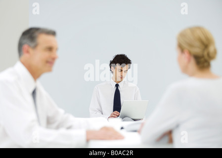 Male professional using laptop computer, colleagues talking in foreground Stock Photo