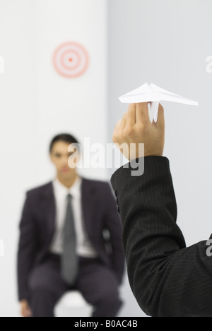 Man holding paper airplane, aiming at target of colleague's head, cropped view Stock Photo