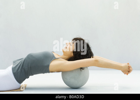 Woman leaning back against fitness ball, arms outstretched, side view Stock Photo