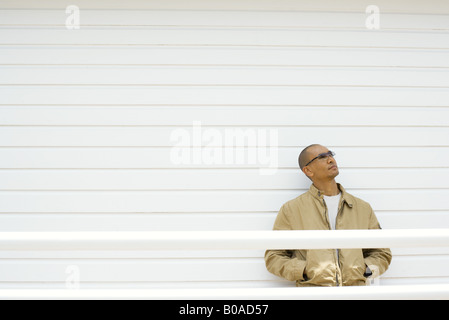 Man leaning against wall, hands in pockets, looking up Stock Photo