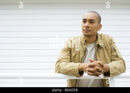 Man leaning against railing with clasped hands, looking away Stock Photo