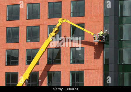 Two construction workers in a cherry picker doing finishing work on a new office block Stock Photo