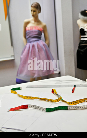 Seen from a sewing workshop. A tape meter placed on a table with various other tools, in the background a dummy wearing a dress. Stock Photo