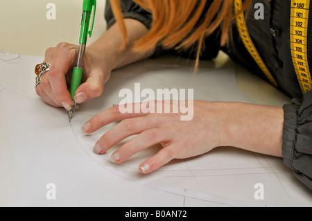 A young seamstress (a tape measure on her shoulders) makes a pattern using a green plastic mechanical pencil. Stock Photo