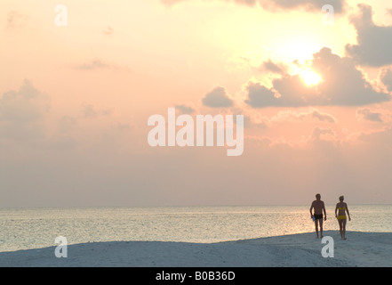 Couples walking into the sunset on Sandspit sandy tropical beach Kuramathi Island Maldives Stock Photo