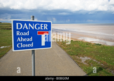 Danger sign on small metalled caravan site road where sea has eroded part of the cliff cutting the road. Stock Photo