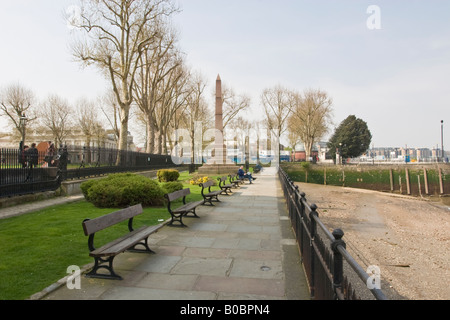 A long line of benches on the Thames path at Greenwich a man relaxes reading a Newspaper Stock Photo