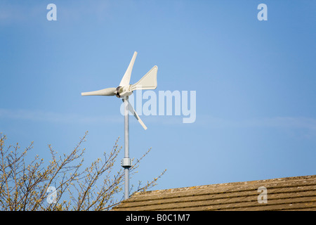Wndsave micro wind turbine mounted on house wall above roof against blue sky Windsave 1200 connects to National Grid blade tail Stock Photo