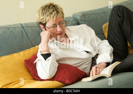 Mature middle aged woman reading a book lying on the sofa at home Stock Photo