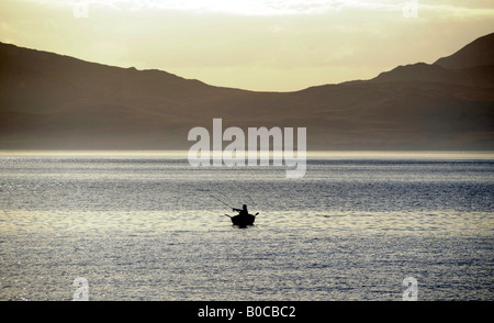 A FISHERMAN FISHES FROM A BOAT IN THE WATERS OFF KINTYRE,NORTH WEST SCOTLAND,LOOKING OUT TOWARDS THE ISLAND OF JURA. Stock Photo