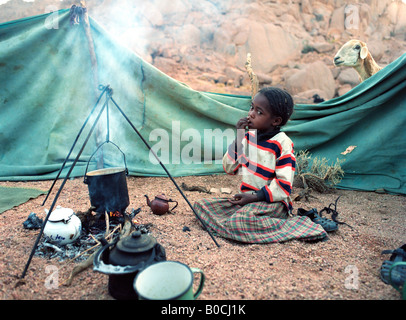 A Tuareg girl is guarding the cooking pot, preparing breakfast in a small settlement in the Ahaggar mountains in South Algeria Stock Photo