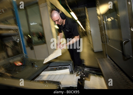 A worker checks copies of newspapers as they are printed on printing presses at Newsfax in East London U K Stock Photo