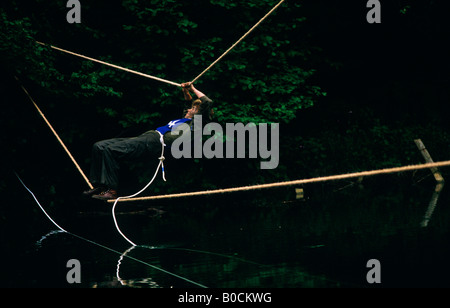 A female member of the Territorial Army hangs on to ropes before falling in pond water during weekend initiative manoeuvres Stock Photo