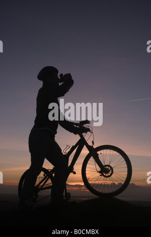 A man silhouetted against the sunset on a mountain bike Stock Photo
