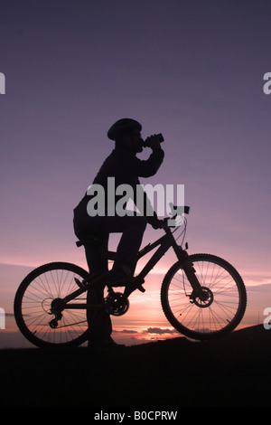 Mountain Biker standing at sunset silhouetted drinking Stock Photo