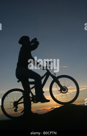 Mountain Biker standing at sunset silhouetted drinking Stock Photo