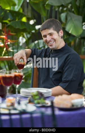 A smiling Spanish chef sits at a colorful table of Mediterranean food. Stock Photo