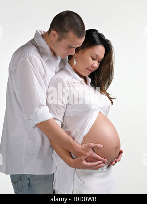 Young multi-racial couple cradling large pregnant womb together Stock Photo