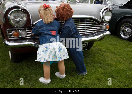 Two life size dolls dressed in 1950s fashion leaning against the radiator grille of a Ford Consul vintage car Stock Photo