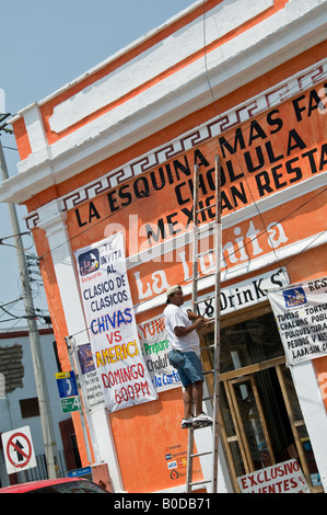 Sign writer stood on a ladder working on painting the new graphics for a Mexican restaurant in Cholula, Mexico. Stock Photo