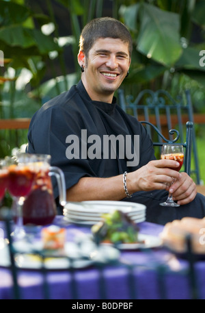 A smiling Spanish chef sits at a colorful table of Mediterranean food. Stock Photo