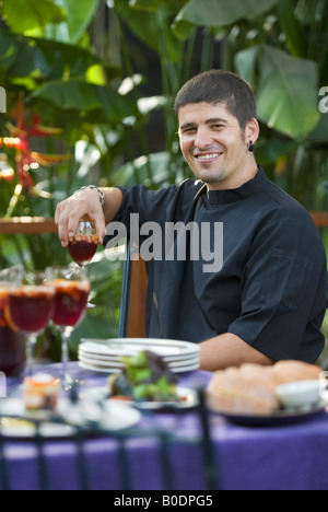 A smiling Spanish chef sits at a colorful table of Mediterranean food. Stock Photo