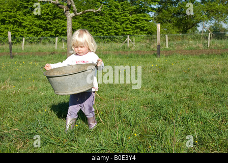 Stock photo of a two year old little girl carrying a metal bowl in her garden Stock Photo
