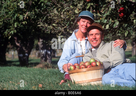 Young adults relax in an orchard after picking a bushel of apples during harvest. Stock Photo