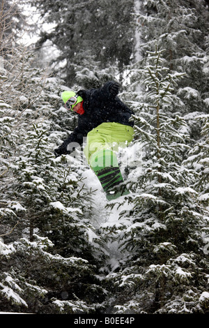 Snowboarder Zac Burke riding off piste jumps though pine trees in the Alps. Stock Photo