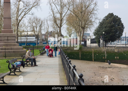 A young woman lies on a bench while her boyfriend sits alongside Three women walk with children in a pushchair Stock Photo