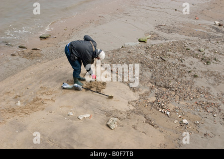 metal Detectorist searches the Foreshore near Greenwich Pier Bends to search a pile of sand in more detail Stock Photo