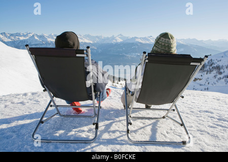 Man, woman relax on deck chairs in snow Stock Photo