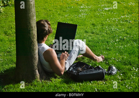 Girl using laptop by tree in park Vienna Austria Stock Photo