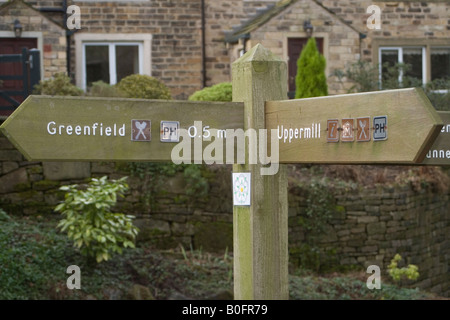 Sign showing the way to Greenfield and Uppermill in Saddleworth, Yorkshire, in front of the stone cottages typical of the region Stock Photo