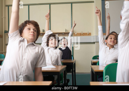 Children raising hands in classroom Stock Photo