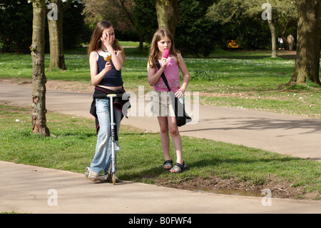 Two young girls eating ice cream on scooter in hot summer sun Vassalls Park Bristol UK Stock Photo