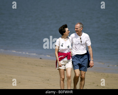 Middle aged couple walking along the seaside, looking lovingly into each others eyes. Stock Photo