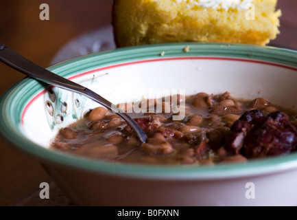 A bowl of cooked pinto beans and ham hock. A piece of cornbread rests against the bowl. Closeup. Southern cuisine, southern cooking. Oklahoma, USA. Stock Photo